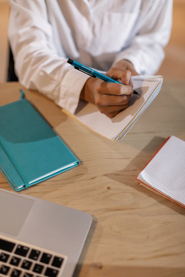 Professional writing notes at a desk while working on a laptop