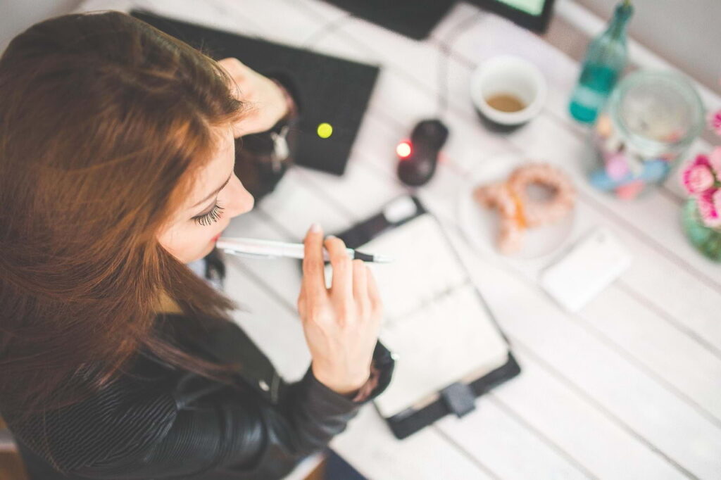 Professional thinking while writing notes at a desk, illustrating unclear communication of work and impact in a LinkedIn experience section