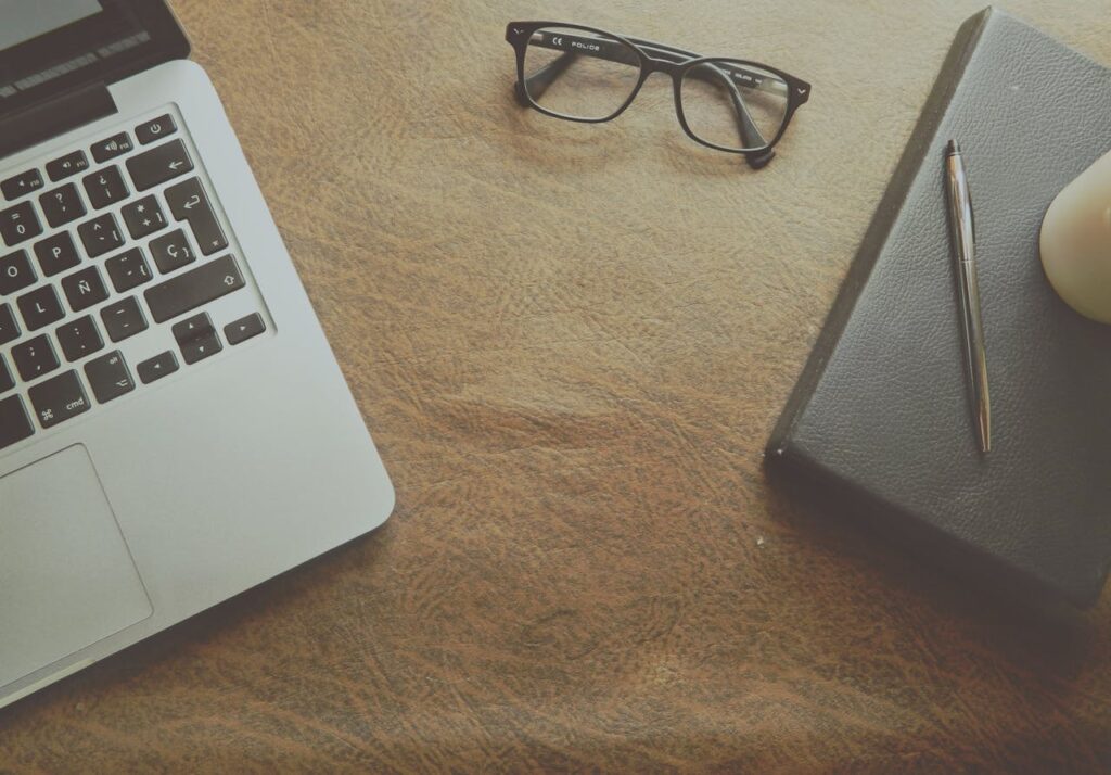 Clean and organized workspace with laptop, notebook, and glasses arranged neatly on a desk
